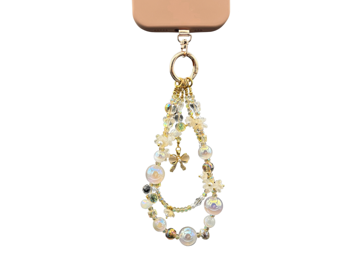 Bracelet Fleur de lait Bloomeliya ivoire, perles nacrées et nœud doré, complet porté sur un téléphone