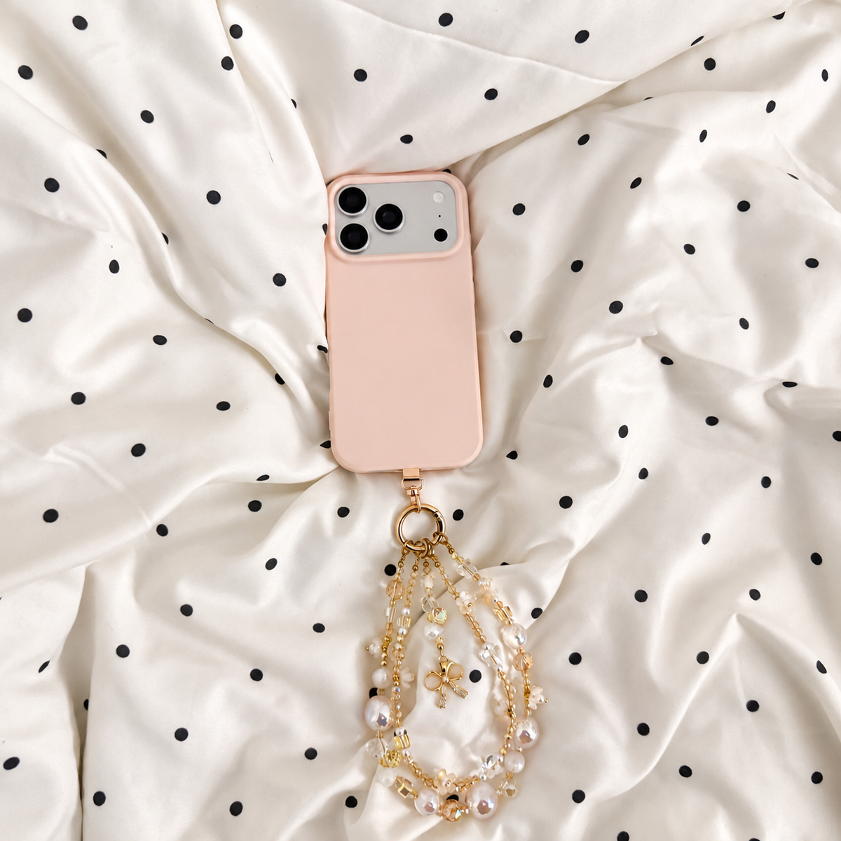 Bracelet Fleur de lait Bloomeliya ivoire, perles nacrées et nœud doré, porté sur un téléphone rose